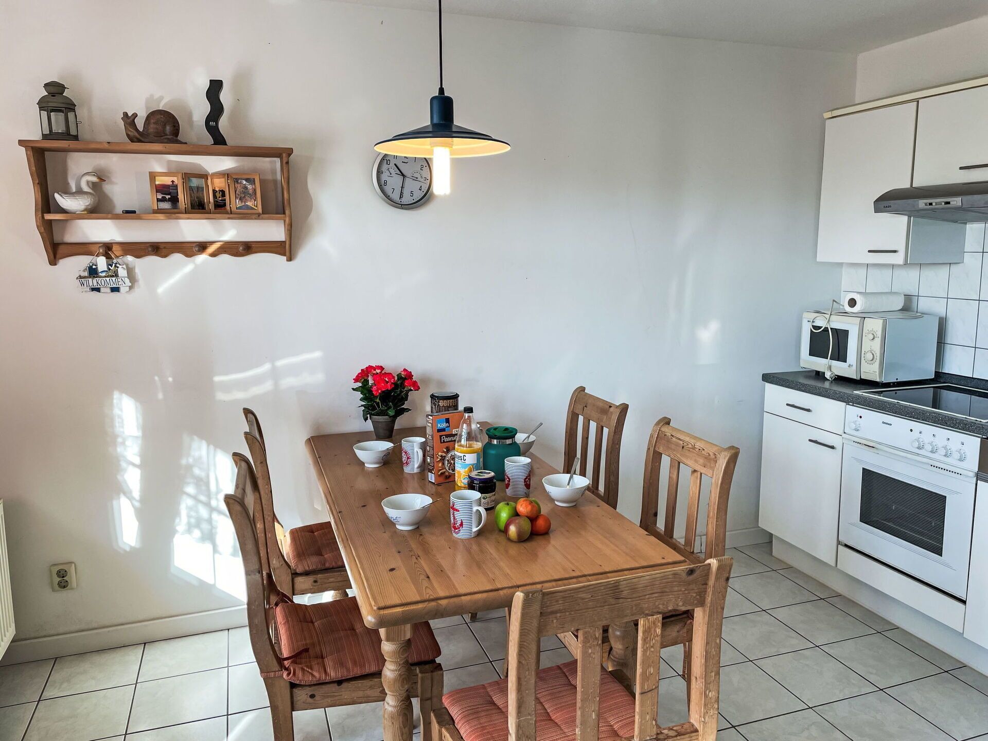 A kitchen with a wooden table, chairs, a clock, and a microwave.