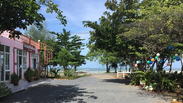 A paved pathway leading to a beach with a pink building on the left and trees on the right. - Ban Chomlay Resort Satun (La-ngu)