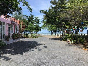 A paved pathway leading to a beach with a pink building on the left and trees on the right. - Ban Chomlay Resort Satun (La-ngu)