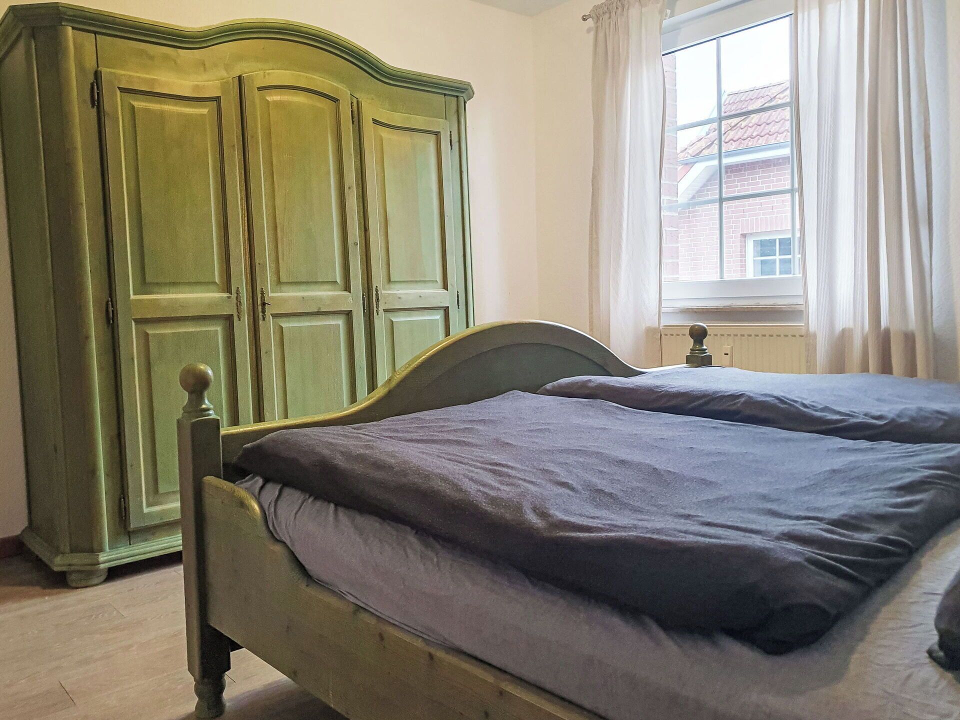 A room with a bed, a wardrobe, and a window with curtains.