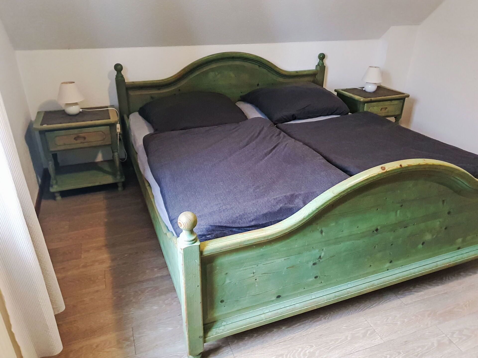A single bed with a wooden frame and a headboard, flanked by two bedside tables with lamps.