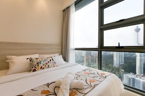 A hotel room with a large bed, a view of tall buildings, and a window with curtains.