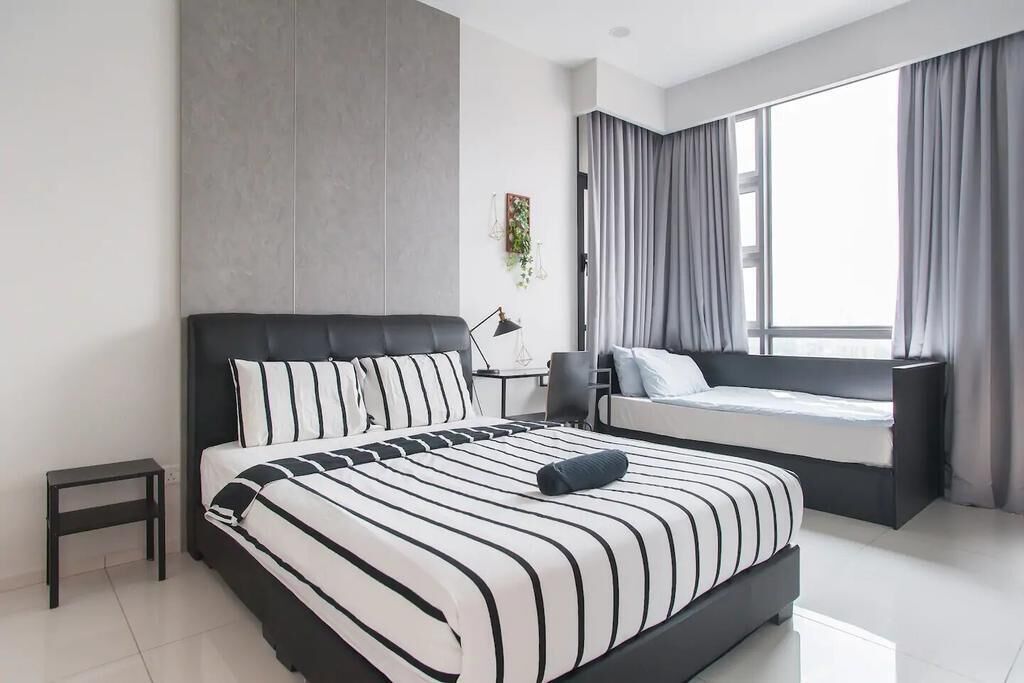 A modern bedroom with a large bed, a bedside table, a small desk, and a window with curtains.