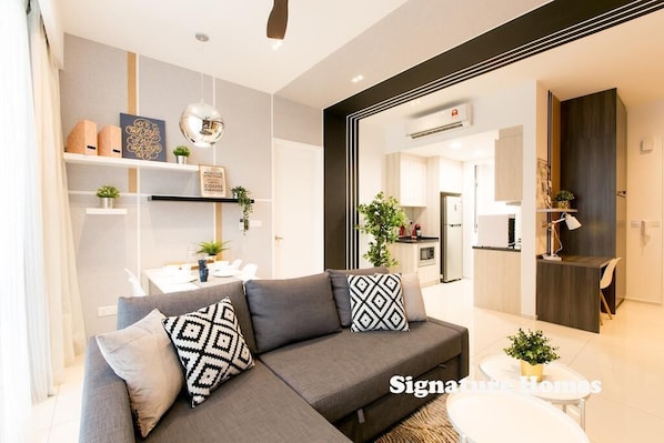 A modern living room with a grey sectional sofa, a small round table, and a kitchen in the background.
