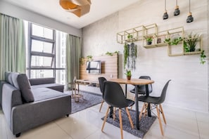 A modern living room with a grey sofa, a dining table with black chairs, and a TV on a wooden wall.