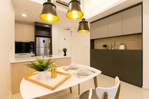 A modern kitchen with a built-in refrigerator, a microwave, and a stove. There is a dining table with a tray, a potted plant, and a gold decorative piece.