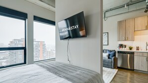 A modern bedroom with a large bed, a TV mounted on the wall, and a view of the city through large windows. - MINNeSTAY* Sable 802 Alcove | North Loop | Target Center (Minneapolis)