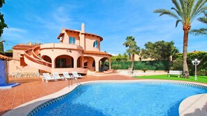 Una amplia piscina de borde curvo, rodeada por una terraza con sillones blancos.