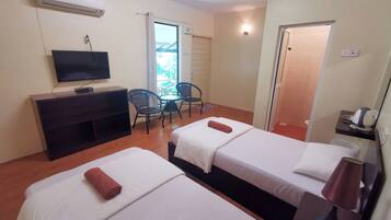 A hotel room with two beds, a TV, a small table with chairs, and a door leading to a balcony.