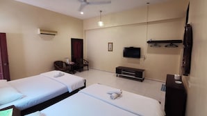 Habitación de hotel con dos camas, televisión, ventilador de techo y un pequeño rincón de descanso.