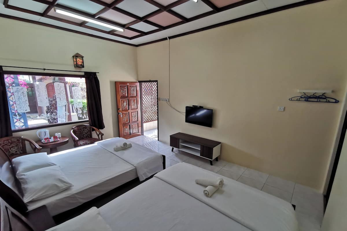 A hotel room with two beds, a TV, a small table with a kettle, chairs, and a view of the outside.