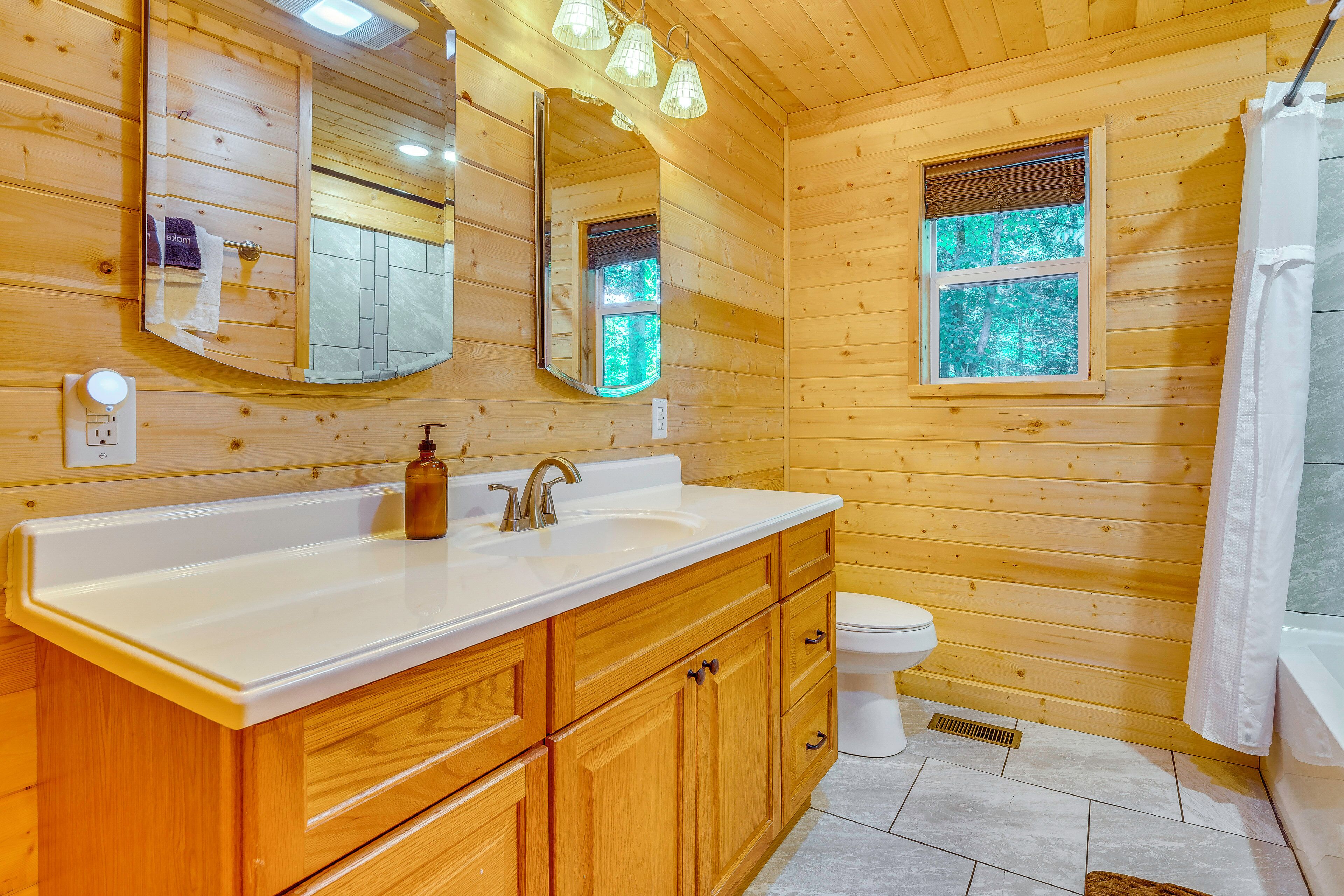 Une salle de bain rustique, aménagée dans une cabane en bois, avec un lavabo, un miroir, des toilettes et une douche.