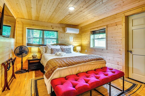 Un dormitorio de cabaña de madera con cama, lámparas de noche, un ventilador y un banco.