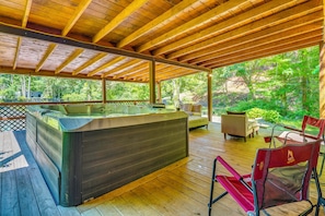 Une terrasse en bois avec un jacuzzi, du mobilier d’extérieur et une vue sur une zone boisée.