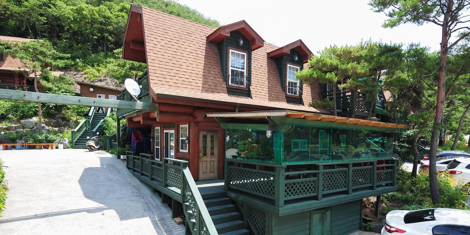 A wooden cabin with a balcony and a glass enclosure, surrounded by greenery.