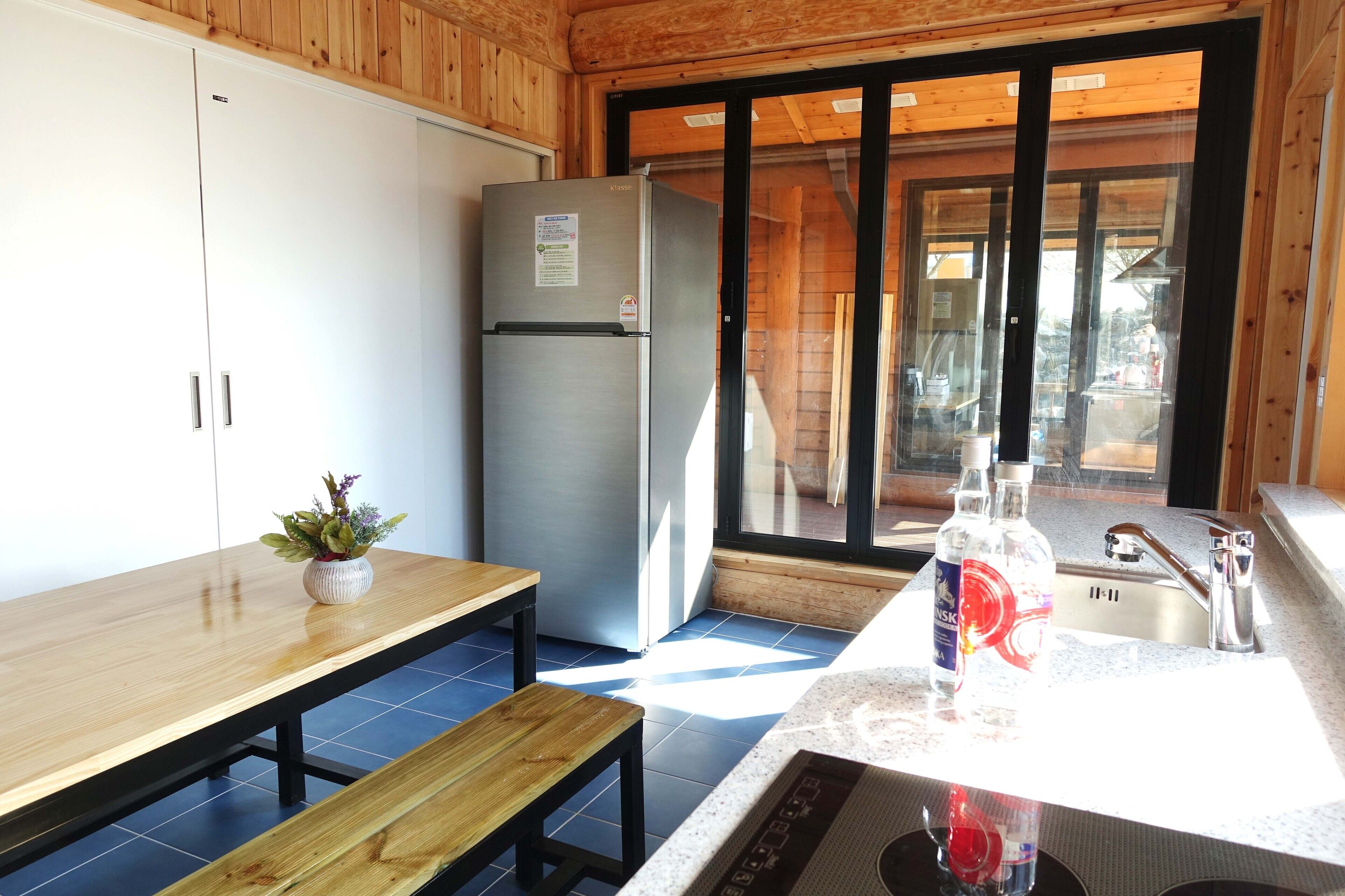 Une cuisine compacte équipée d’un réfrigérateur en acier inoxydable, d’un banc en bois, d’une petite table agrémentée d’une plante en pot et d’un évier avec un robinet.