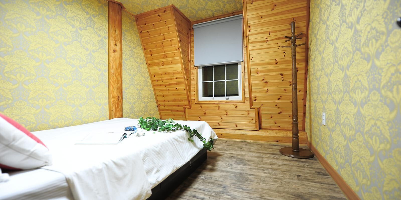 A small, cozy bedroom with a single bed, a window, and wooden walls.