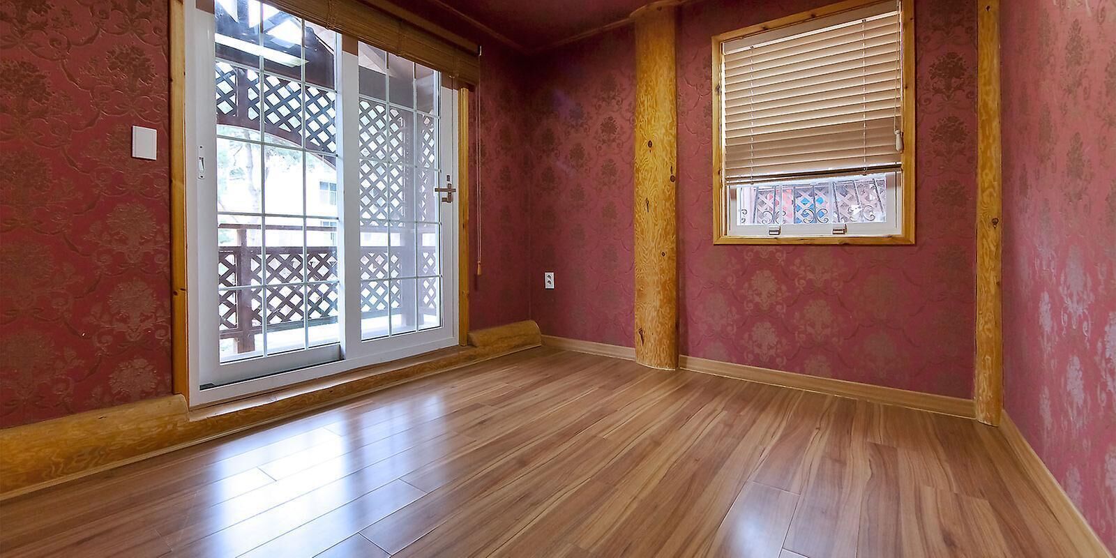 A room with a sliding glass door, a window with blinds, and wooden flooring.