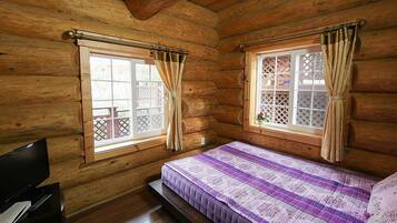 Une chambre aménagée dans un chalet en rondins, avec deux fenêtres, un lit et un bureau équipé d’un ordinateur.