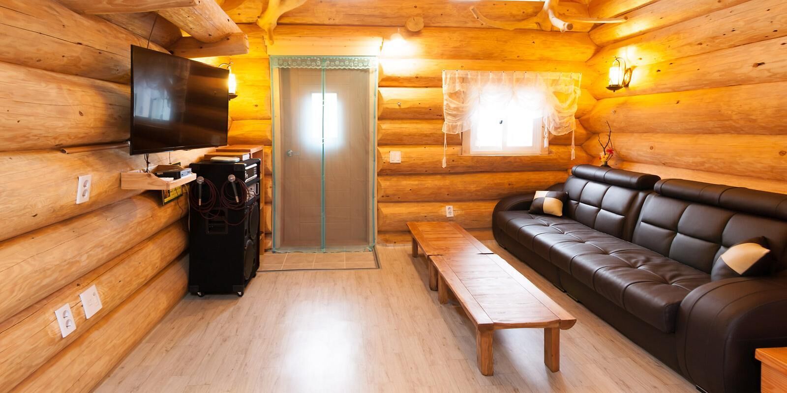 Interior de una cabaña de troncos con un sofá, un televisor, una mesa de madera y una puerta corredera.