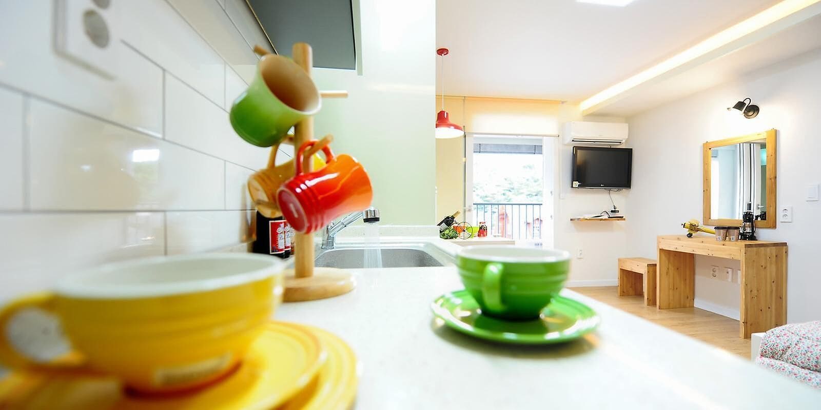 A modern kitchen with white tiles, a wooden countertop, and a TV mounted on the wall.