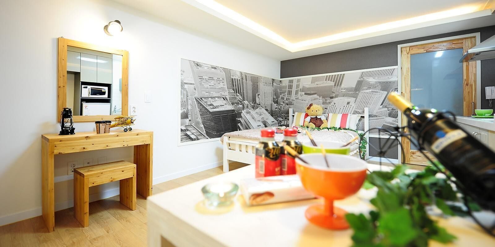 Una cocina moderna con un banco de madera, una mesa de comedor con un osito de peluche y un cuadro grande de un paisaje urbano en blanco y negro en la pared.