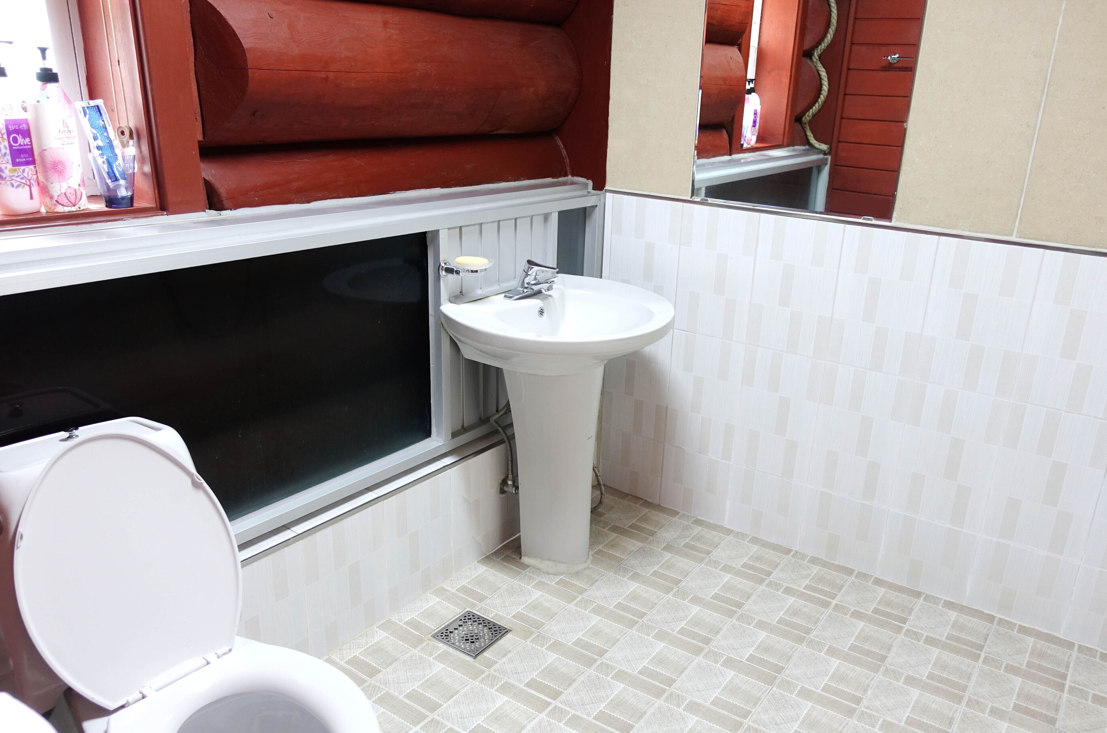Une salle de bain avec des toilettes blanches, un lavabo et une fenêtre.