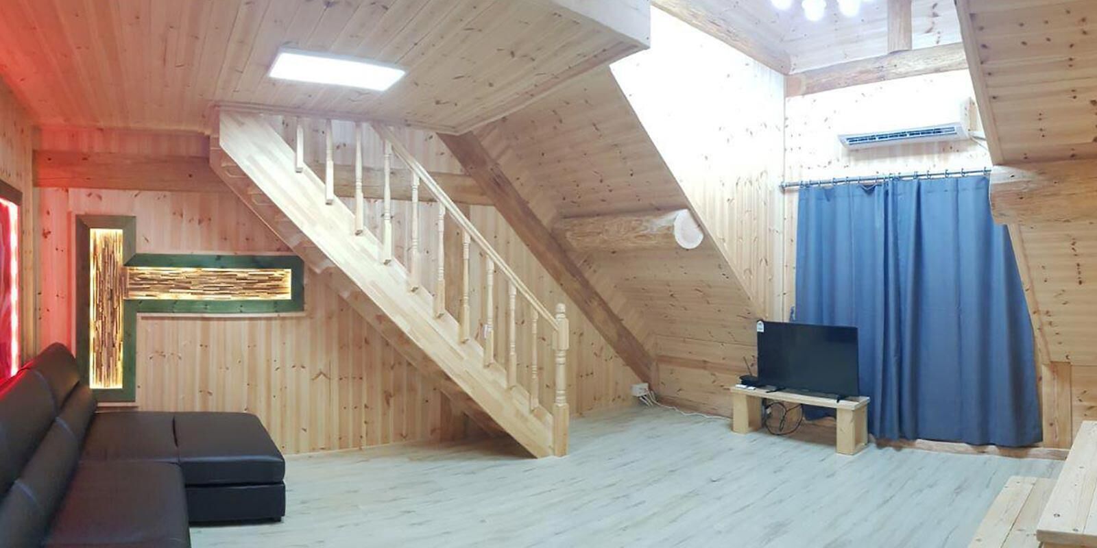 Un interior de madera con una escalera, un sofá, un televisor y una ventana con cortinas.