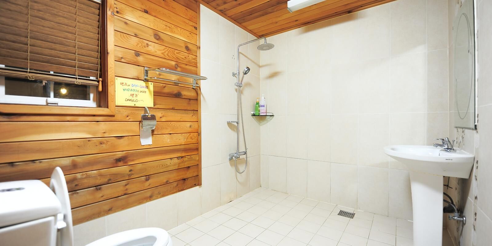 Une salle de bain avec des murs en bois, une douche, un lavabo et des toilettes.