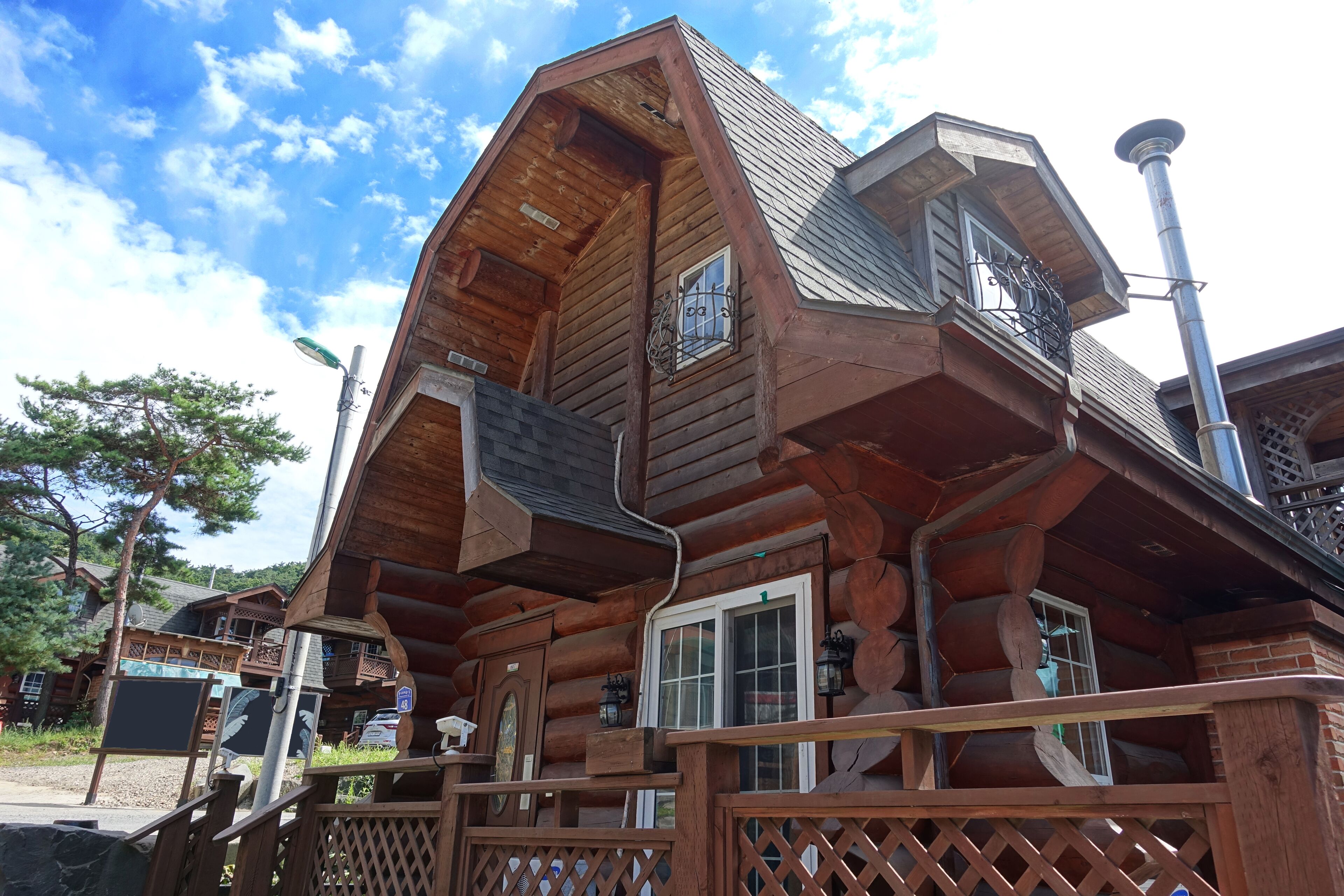 A wooden log cabin with a balcony, a chimney, and a signboard.