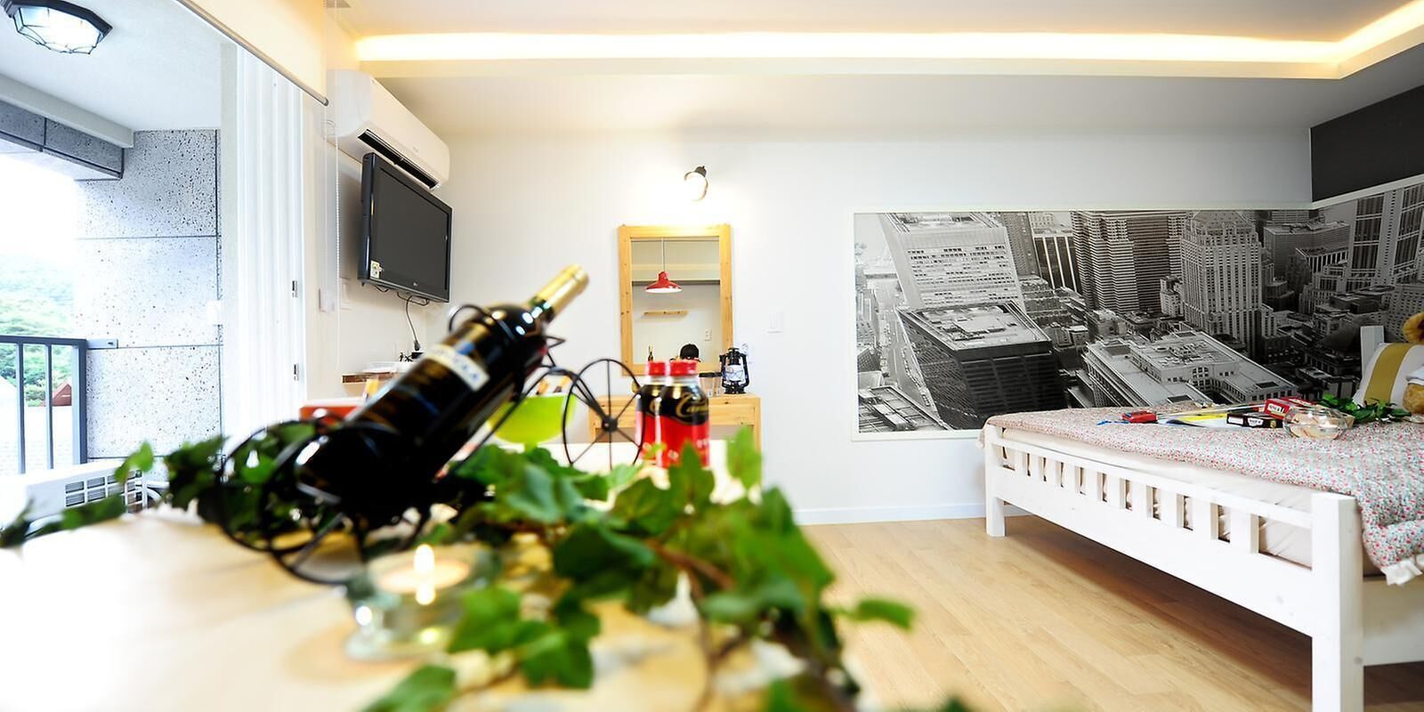 Un dormitori modern amb un llit blanc, un mural amb un paisatge urbà, una televisió i un balcó amb vistes.