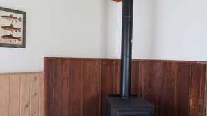 A room with a wood-burning stove, wooden walls, and a tiled floor. - Hunting ~n~ Hooks Getaway (Salmon)