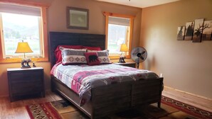 A bedroom with a bed, two nightstands, a floor lamp, a wall-mounted fan, and a window with a view of the outdoors. - Hunting ~n~ Hooks Getaway (Salmon)