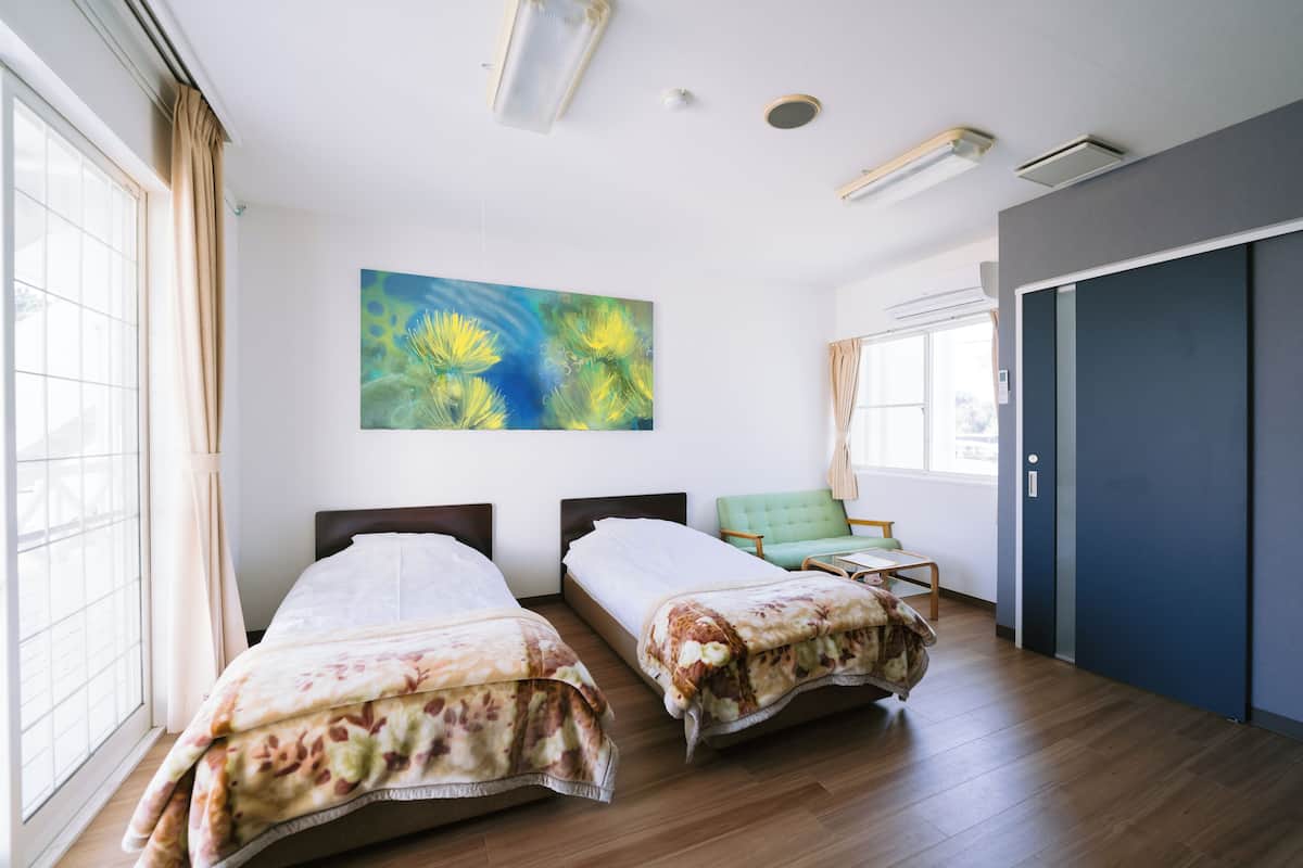 A hotel room with two beds, a large window, a painting, and a door.