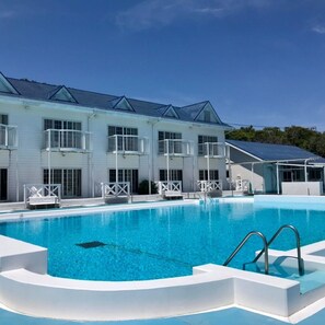 A swimming pool with a white building in the background, featuring balconies and a covered area. - Hotel Kailani (Oshima)