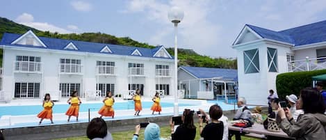 Un grupo de bailarines actuando en un escenario frente a un edificio con piscina.