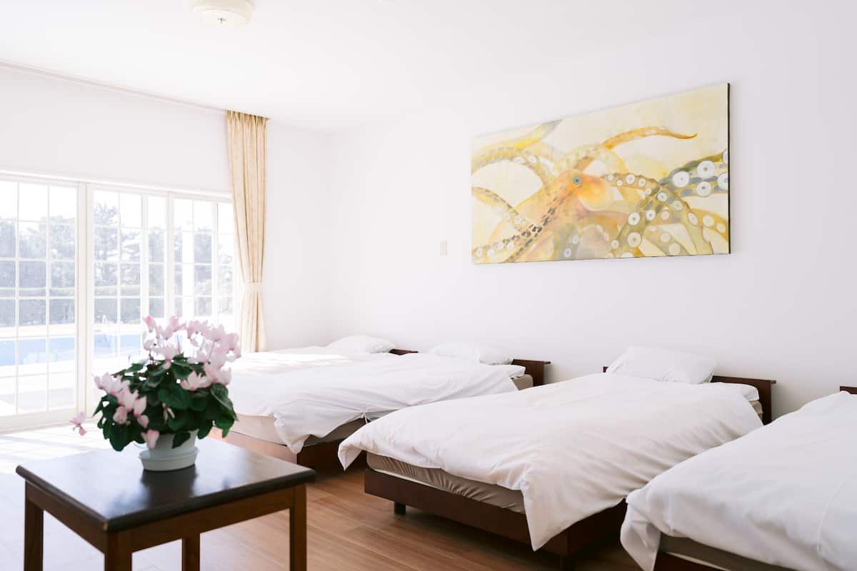 A hotel room with three beds, a large window, and a painting on the wall.