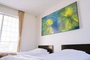 Habitación de hotel con dos camas, un cuadro abstracto grande en la pared y una ventana con cortinas.