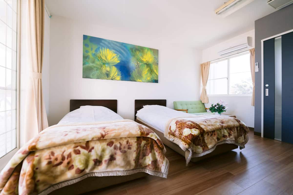 A hotel room with two beds, a large window, a painting on the wall, and a door.
