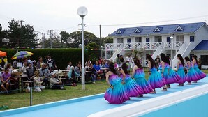 A group of women in colorful dresses performing in front of an audience at an outdoor event. - Hotel Kailani (Oshima)