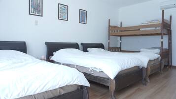 Una habitación con literas y dos camas individuales, ropa de cama blanca y cuadros en la pared.