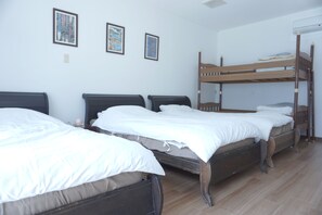 Une chambre avec des lits superposés et deux lits simples, du linge de lit blanc et des tableaux encadrés accrochés au mur.