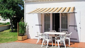 Un bâtiment blanc avec un toit en tuiles, un patio couvert avec une table et des chaises, et un jardinier en bois.