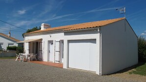 Il s’agit d’un petit bâtiment d’un seul étage, à l’extérieur blanc et doté d’un toit recouvert de tuiles. Il possède une porte de garage et un petit patio avec une table et des chaises.
