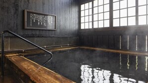 Un onsen japonés tradicional con interiores de madera, una pared de piedra y un ventanal grande.