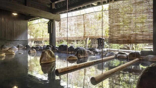 Un baño termal tradicional con vigas de madera, rocas y paneles de bambú.