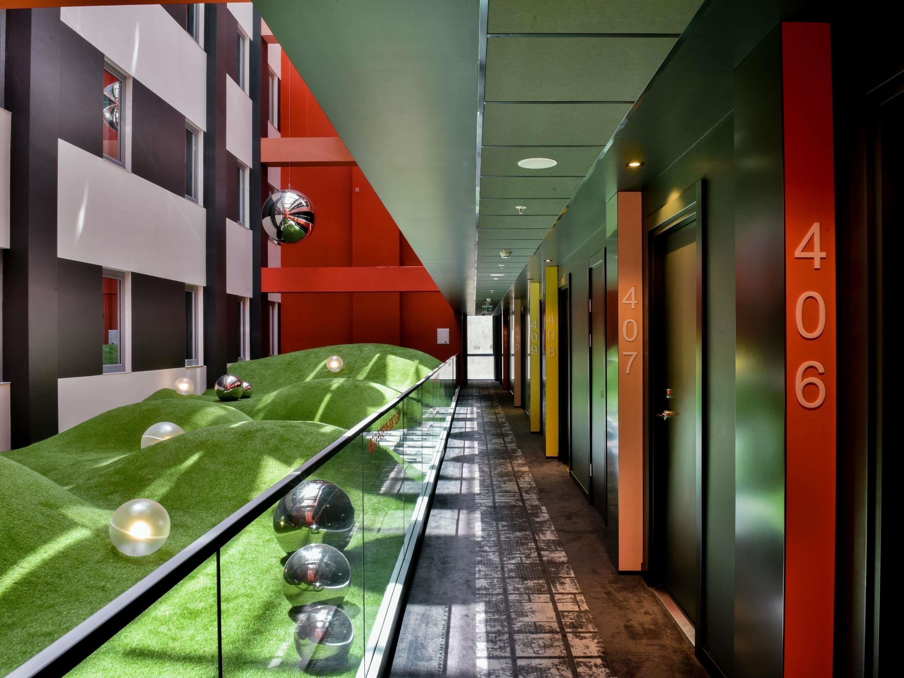 A corridor with a green artificial turf, glass railings, and doors numbered 406 to 410.