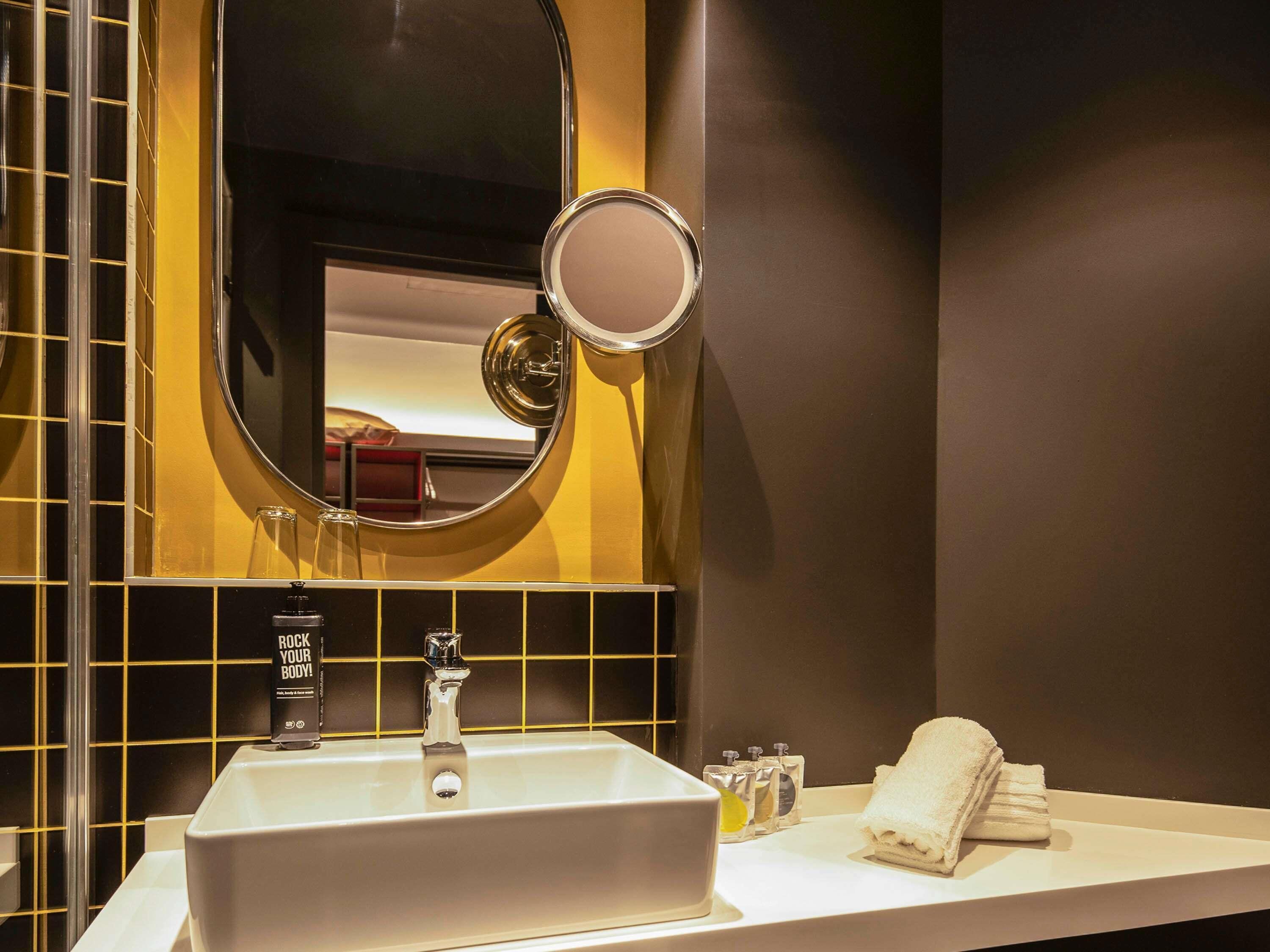 A bathroom with a large oval mirror, a sink, a towel rack, and toiletries.
