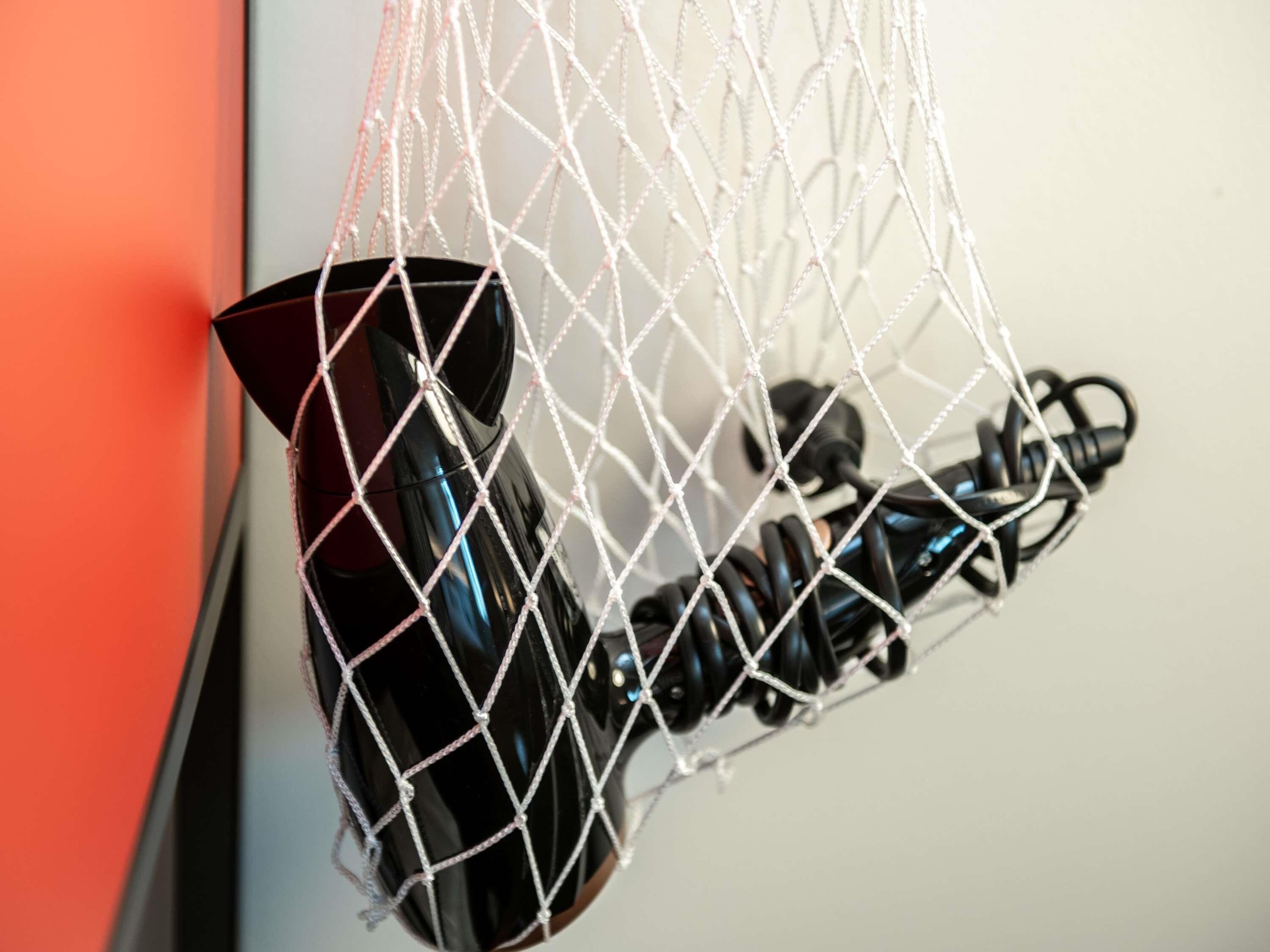 A black object, possibly a speaker, hanging from a white net against a wall.