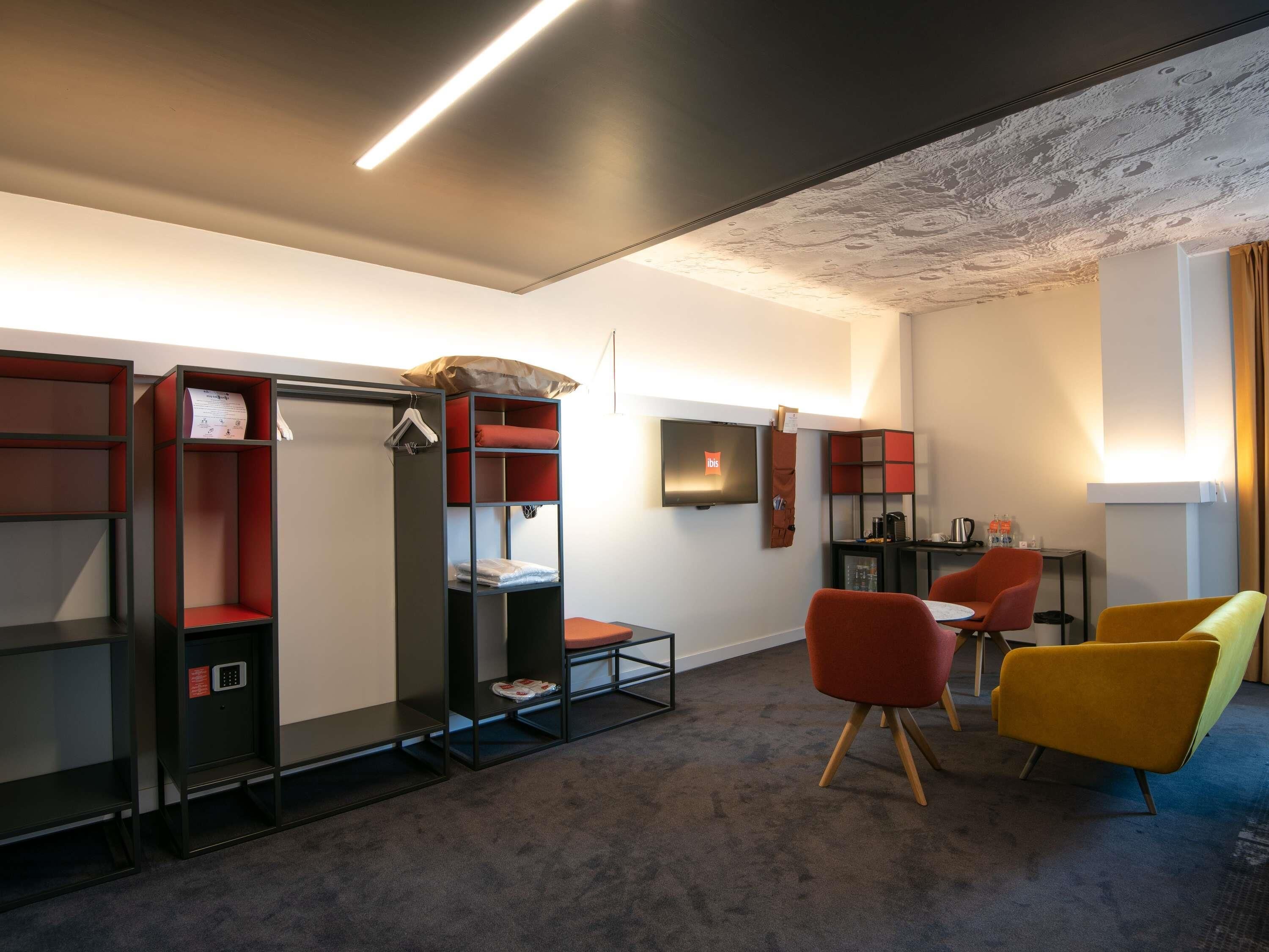 A modern hotel room with a flat-screen TV, built-in shelves, a desk, and a sofa.